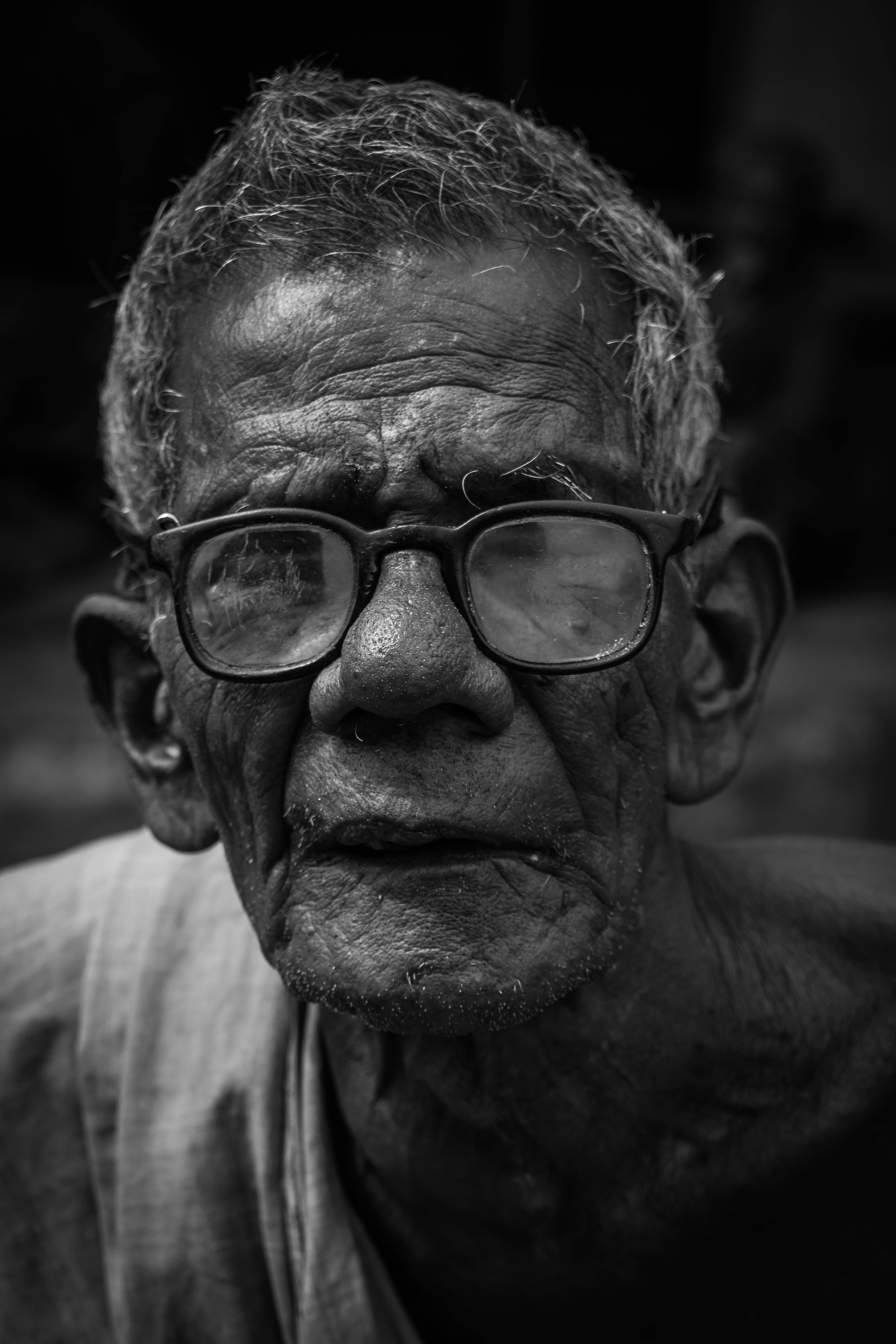 黑白 桌布 壁紙 — 一位滿臉皺紋、戴著眼鏡的長者，近距離黑白肖像，專注地凝視鏡頭。
