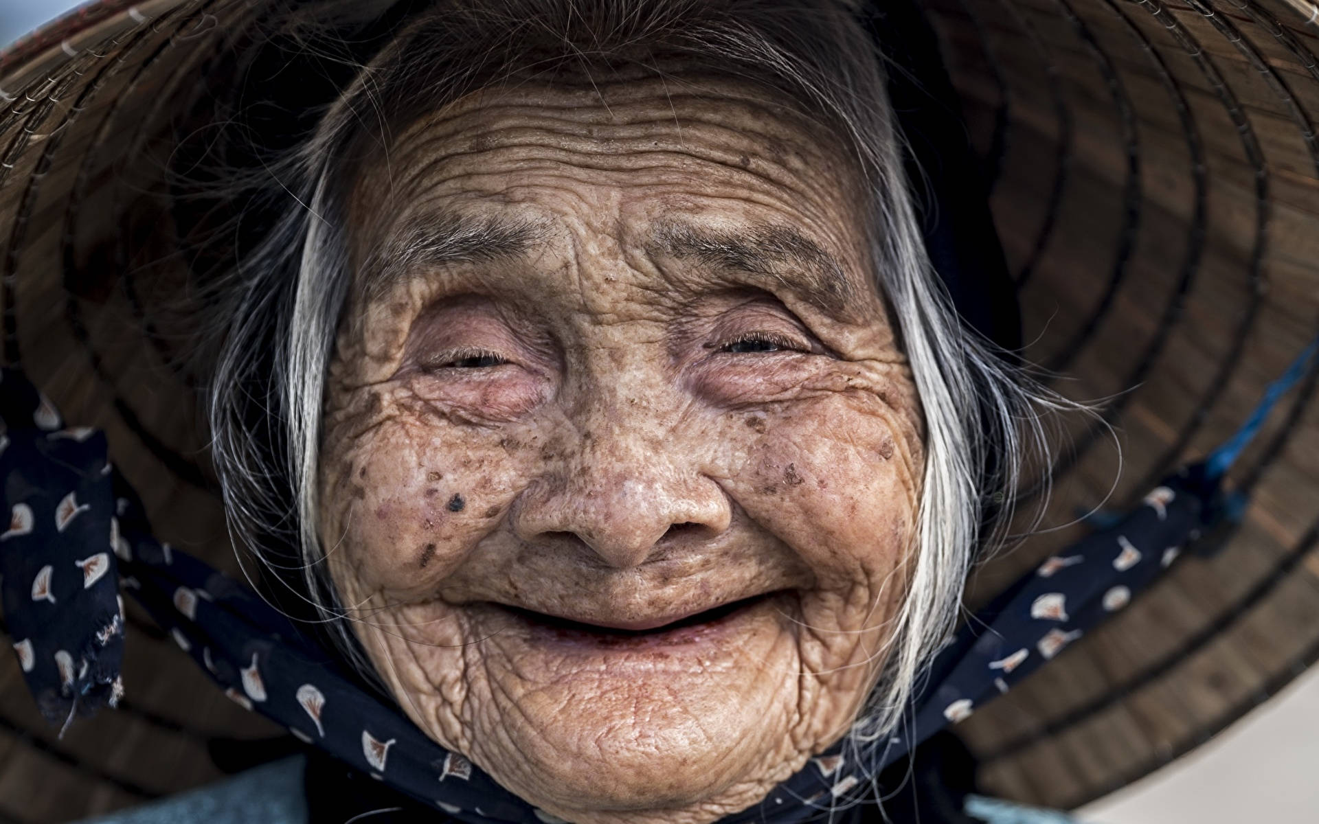 笑臉 桌布 壁紙 — 一位滿臉皺紋、笑容燦爛的老年婦女戴著編織草帽的特寫。