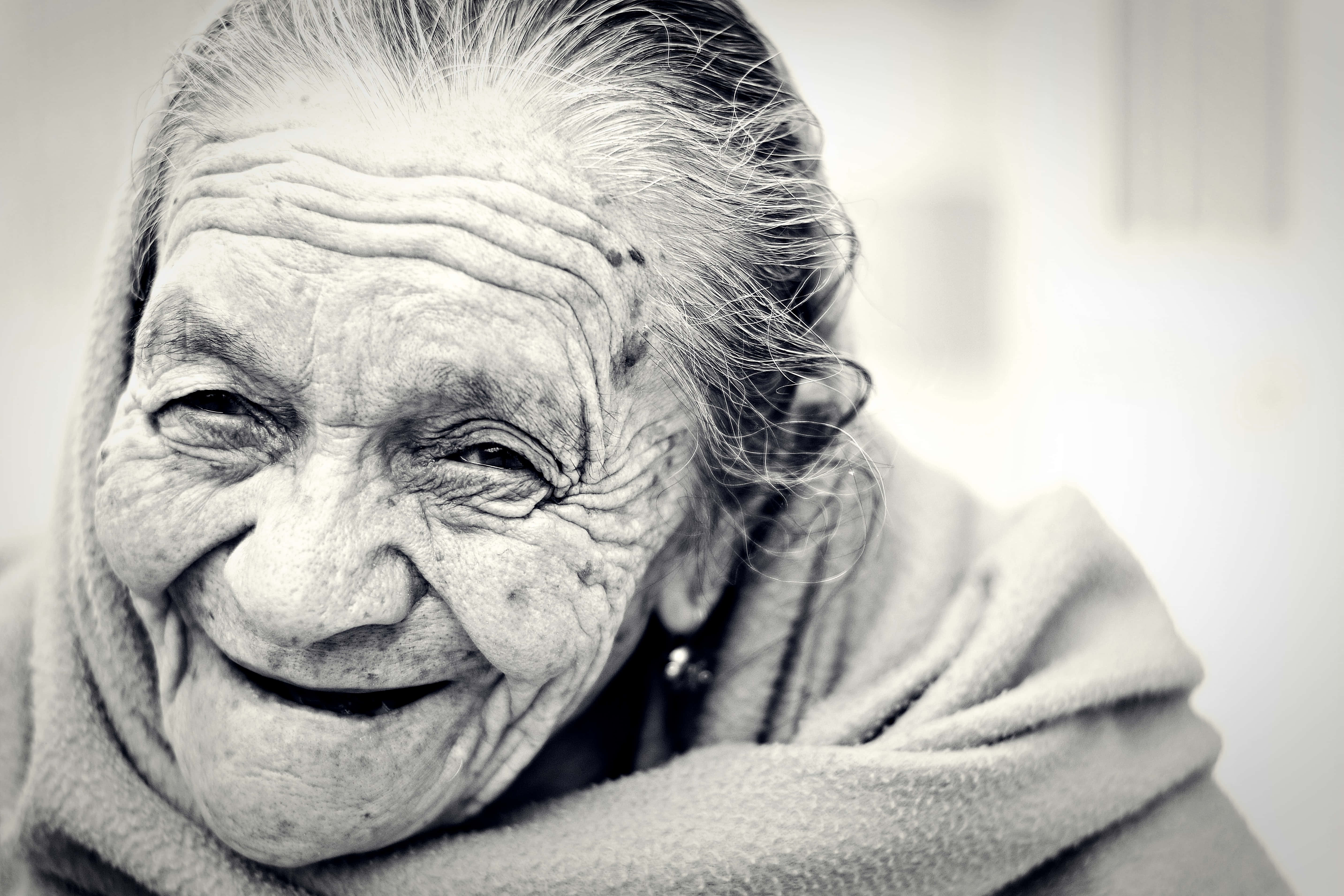 Mature 桌布 壁紙 — 一位滿臉皺紋的老婦人微笑著包裹在柔軟毯子中的黑白特寫肖像。