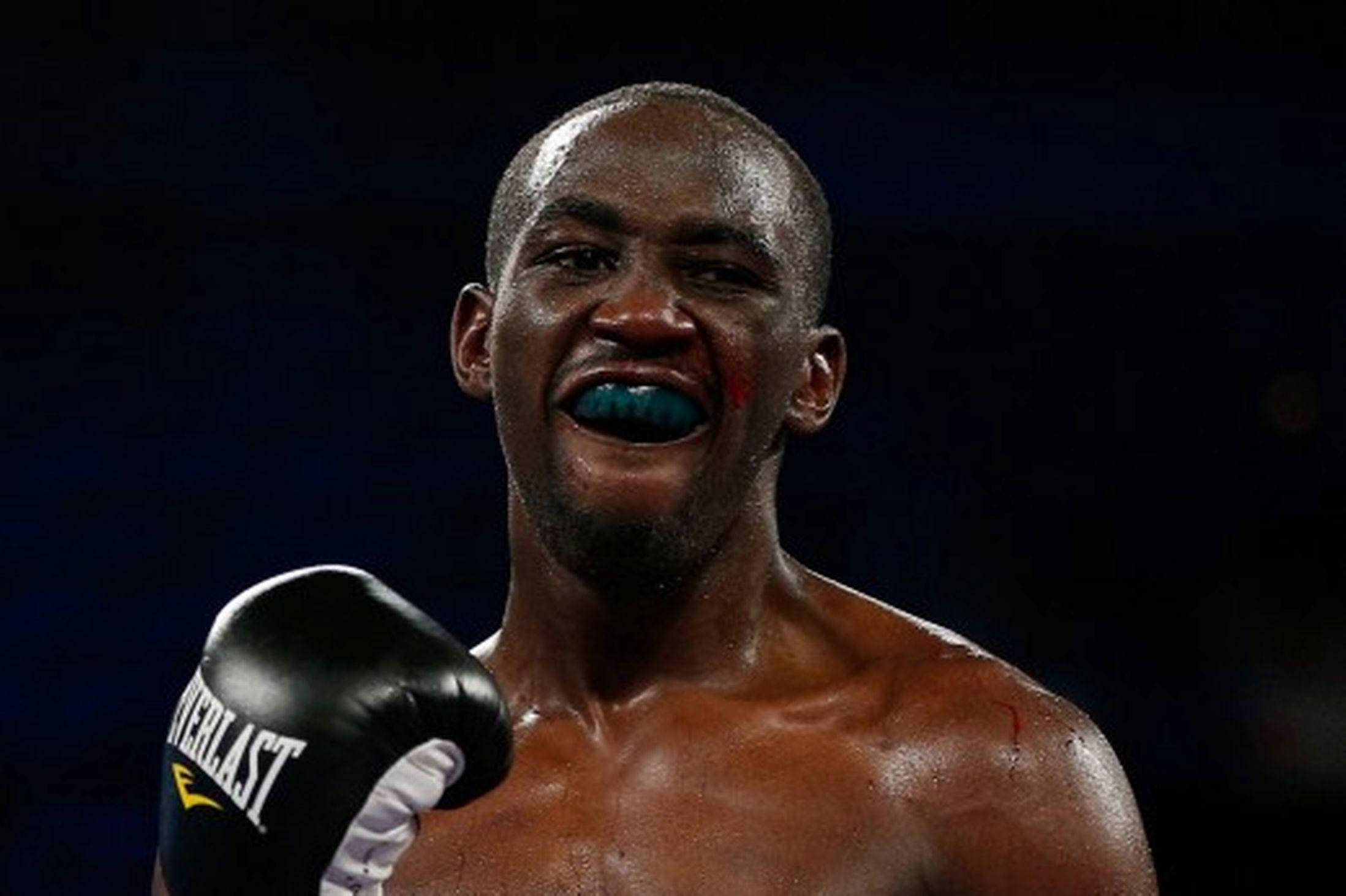 Boxing 桌布 壁紙 — 一位滿臉鮮血、戴著藍色護齒的勝利拳擊手在競技場燈光下咆哮勝利。