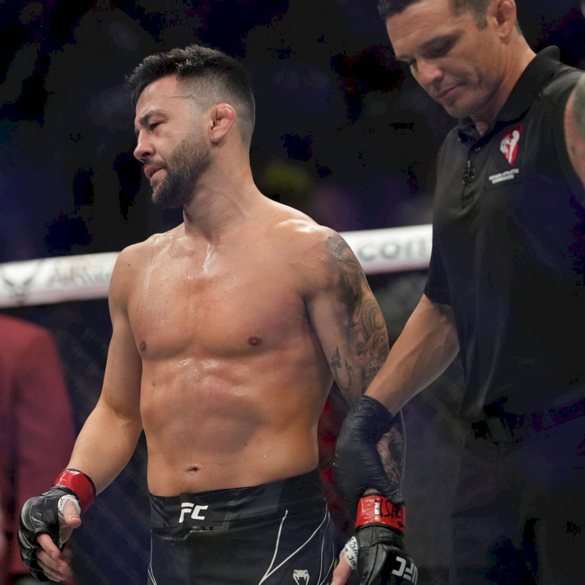 Champion 桌布 壁紙 — 一位滿身大汗、帶有刺青的UFC拳手站在八角籠中，裁判在比賽後扶著他的手臂。