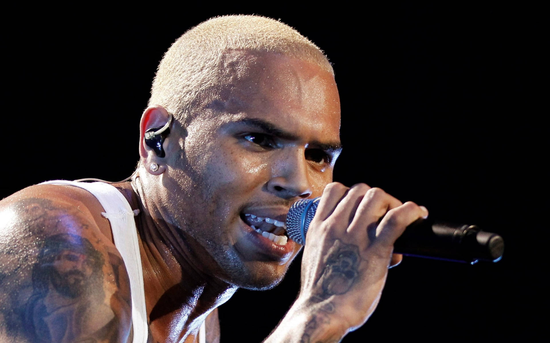 Chris Brown 桌布 壁紙 — 一位滿頭大汗、剃光頭、有刺青的男歌手，在黑色背景前熱情地對著麥克風演唱。
