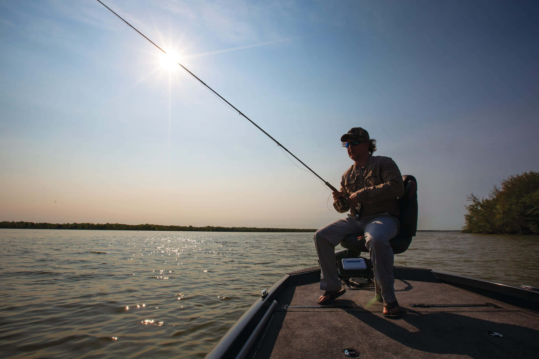 Fishing Bait 桌布 壁紙 — 一位漁夫坐在船上拋出釣線，夕陽在平靜的水面上明亮地照耀。