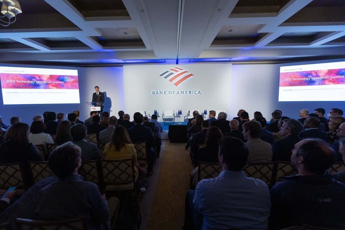 Bank Of America 桌布 壁紙 — 一位演講者在Bank of America Technology Innovation Summit上，向現代會議廳中帶有藍色環境照明的觀眾進行演講。