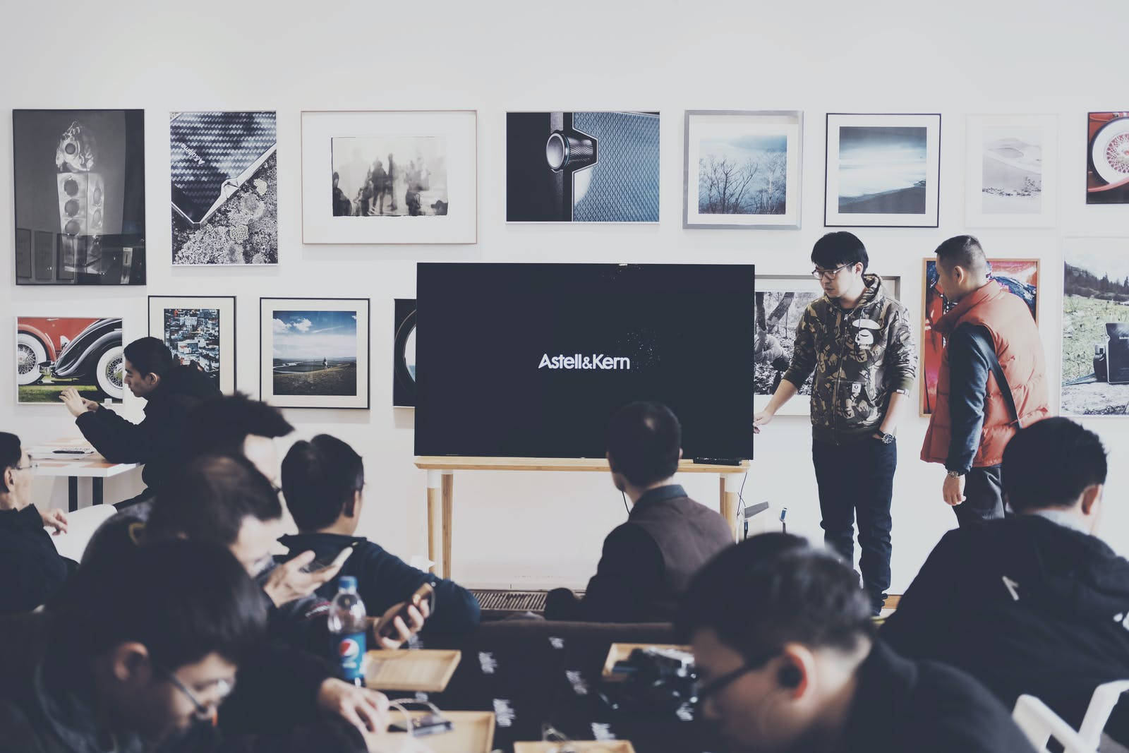 Education 桌布 壁紙 — 一位演講者站在觀眾面前，在一個現代的房間裡，牆上掛著裱框藝術品，屏幕上顯示著AstellKern。
