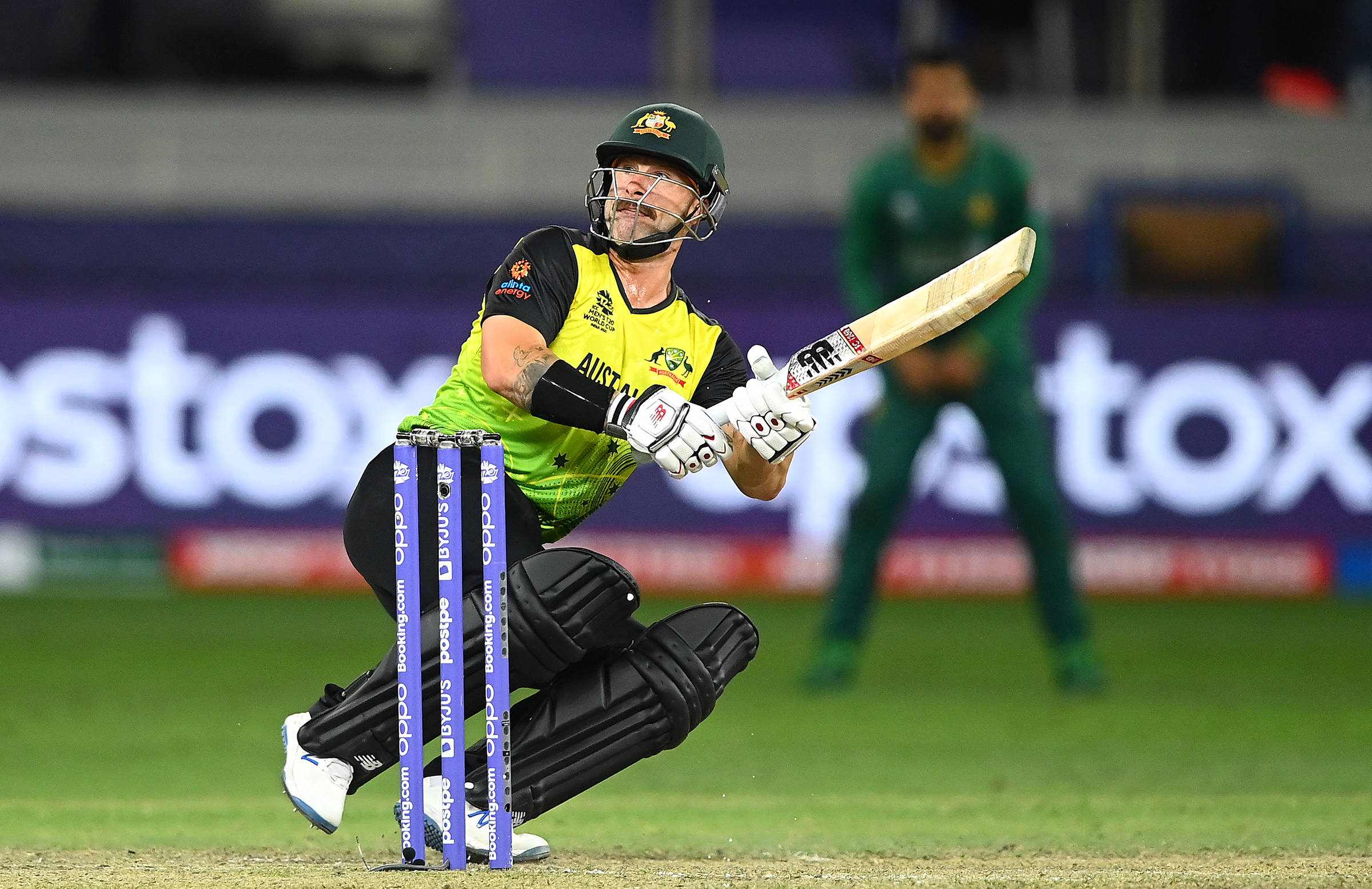 australia cricket 桌布 壁紙 — 一位澳洲板球擊球手穿著綠色和金色的裝備，在夜間比賽中於體育場燈光下強力揮動球棒。
