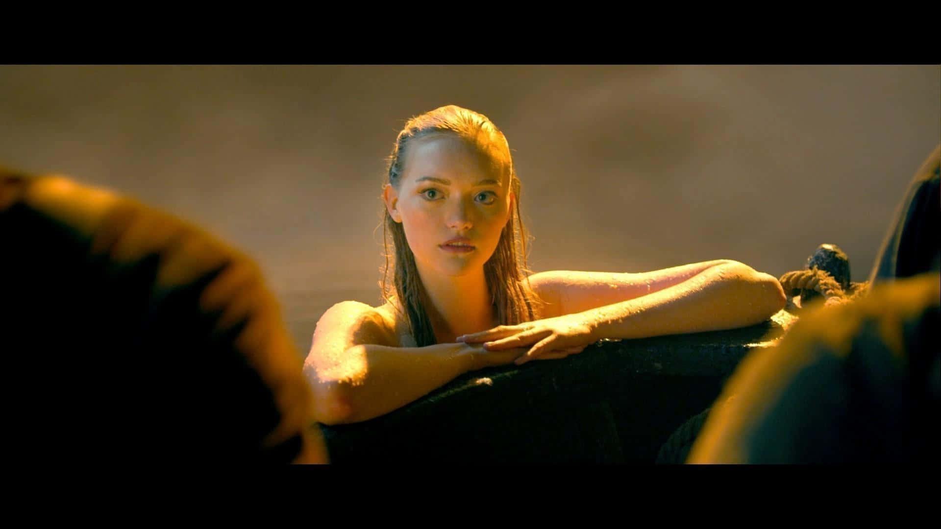 Gemma Ward 桌布 壁紙 — 一位濕髮女士俯身於一個黑暗的表面上，沐浴在溫暖的金色光線中，背景朦朧。