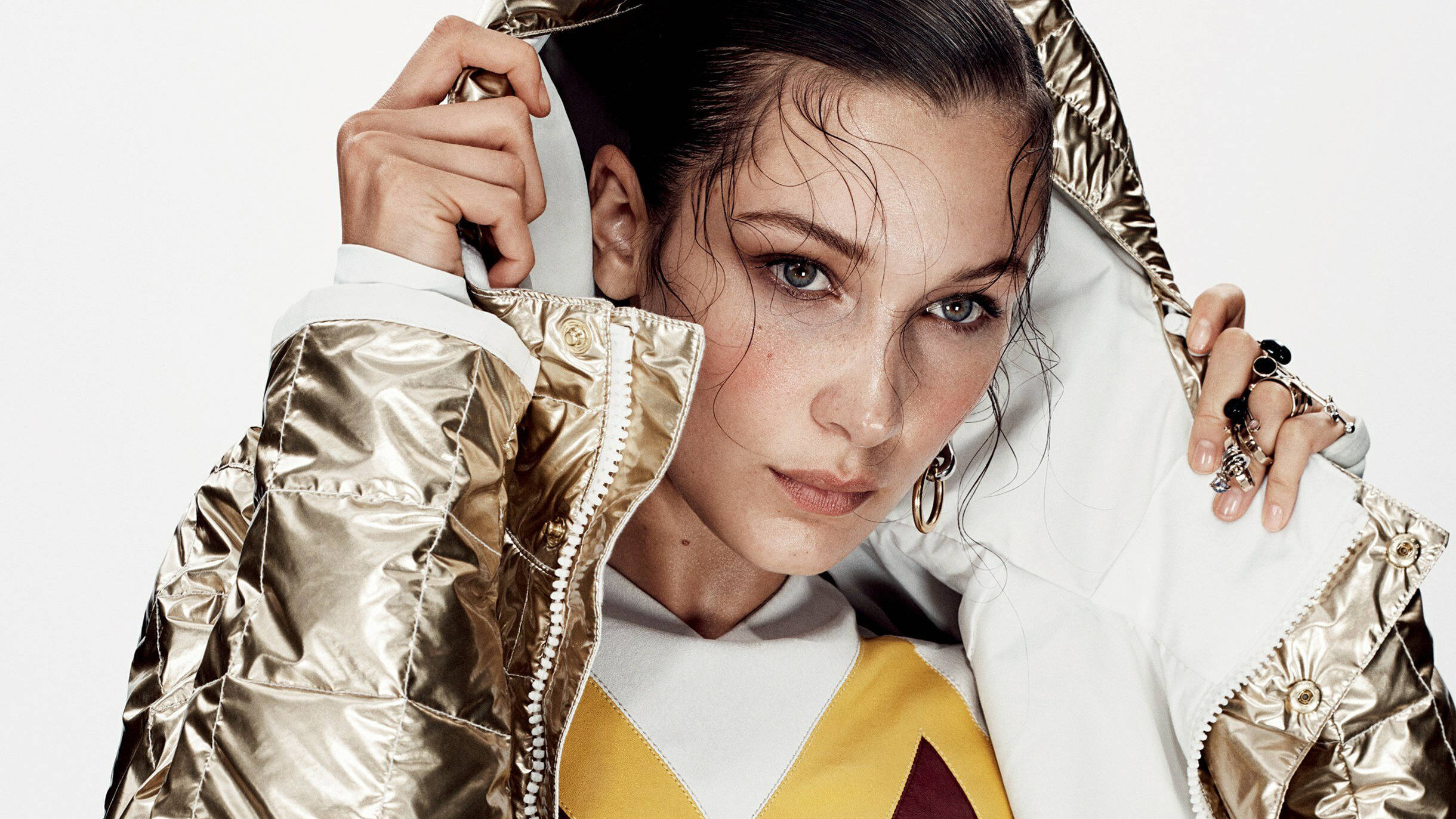 Bella Hadid 桌布 壁紙 — 一位濕髮女子拉起閃亮金白色外套的帽子，凝視著鏡頭。