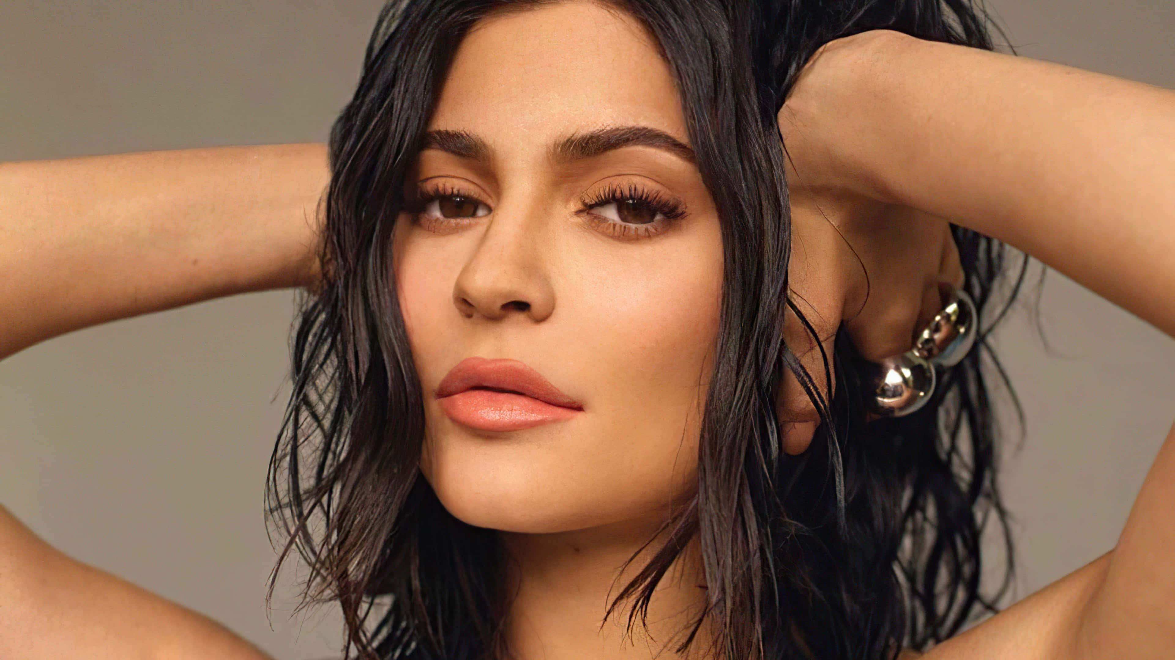 Kylie Jenner 4K 桌布 壁紙 — 一位濕黑頭髮、濃妝豔抹的女性雙手放在腦後擺姿勢的特寫肖像。