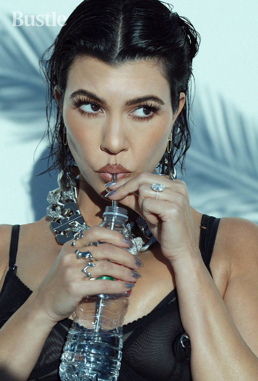 Kourtney 桌布 壁紙 — 一位濕黑髮女性透過吸管喝水，佩戴大膽的銀飾和黑色內衣，背景為棕櫚葉。