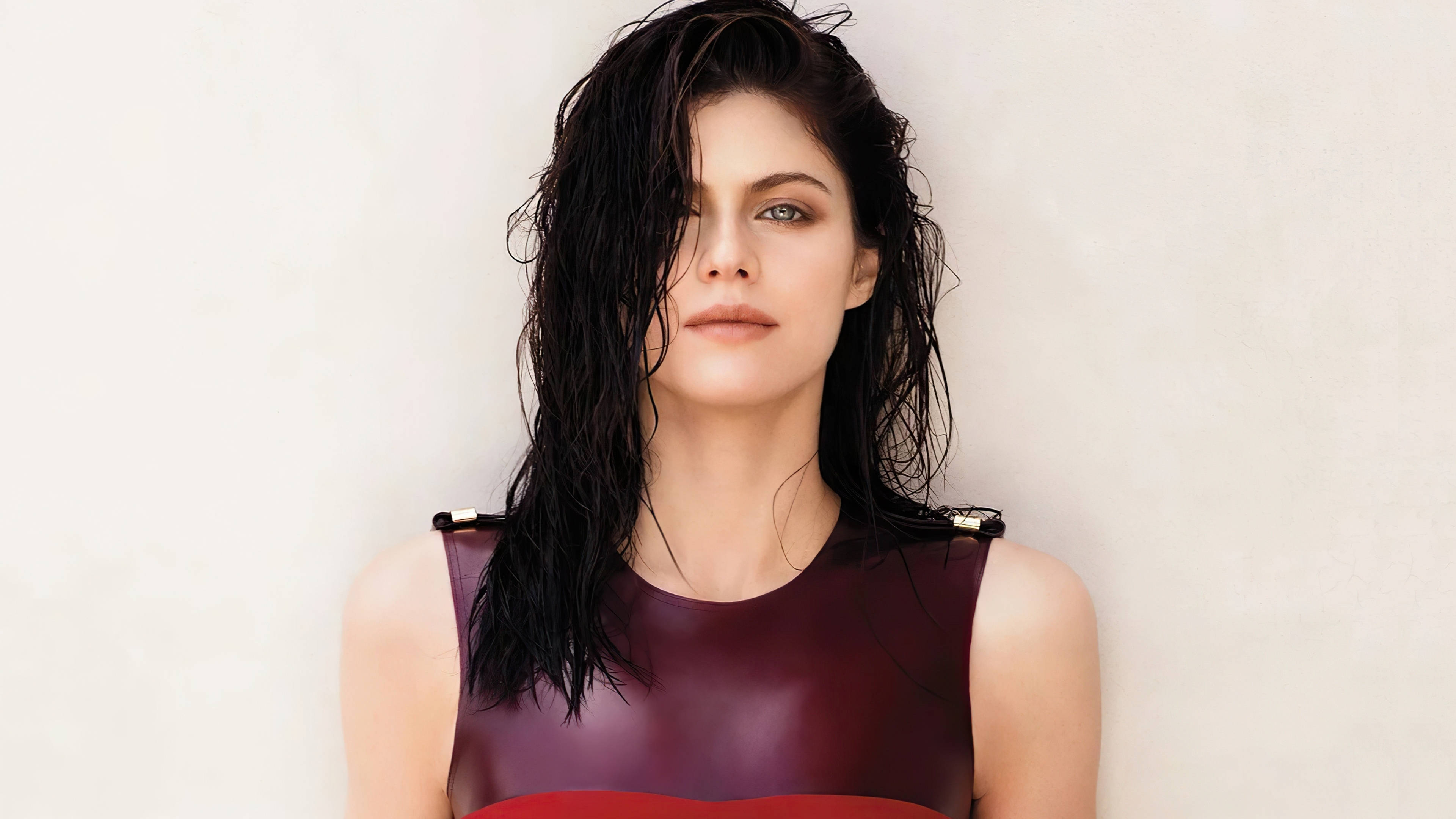 Alexandra Daddario 4K 桌布 壁紙 — 一位濕黑髮的女性靠著素牆，身穿亮面栗色和紅色上衣。