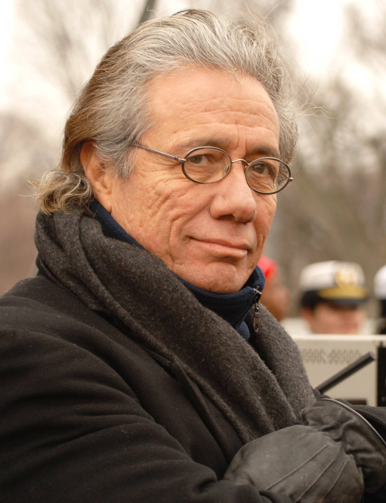 actor 桌布 壁紙 — 一位灰白頭髮、戴圓框眼鏡的長者，穿著深色外套和圍巾，若有所思地看著鏡頭。
