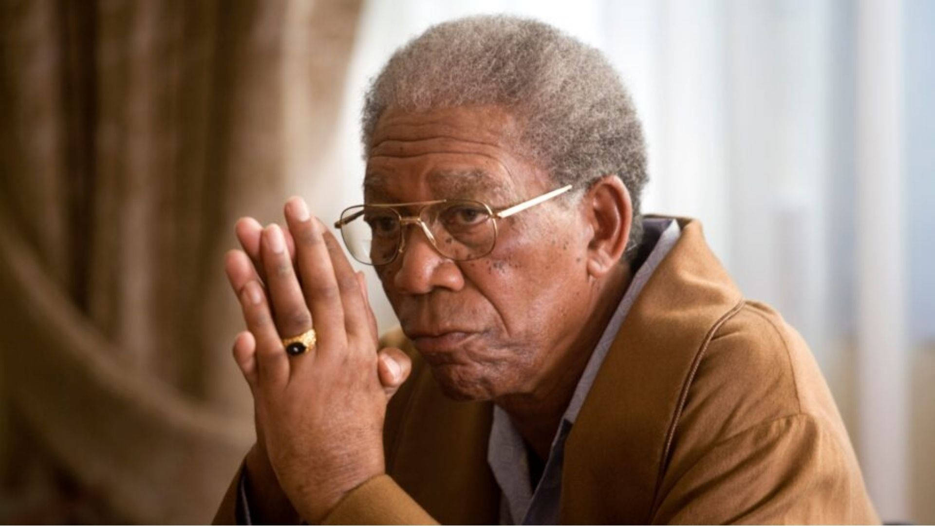 Morgan Freeman 桌布 壁紙 — 一位灰白頭髮、戴眼鏡的長者，雙手交握靠近臉龐，擺出沉思的姿勢。