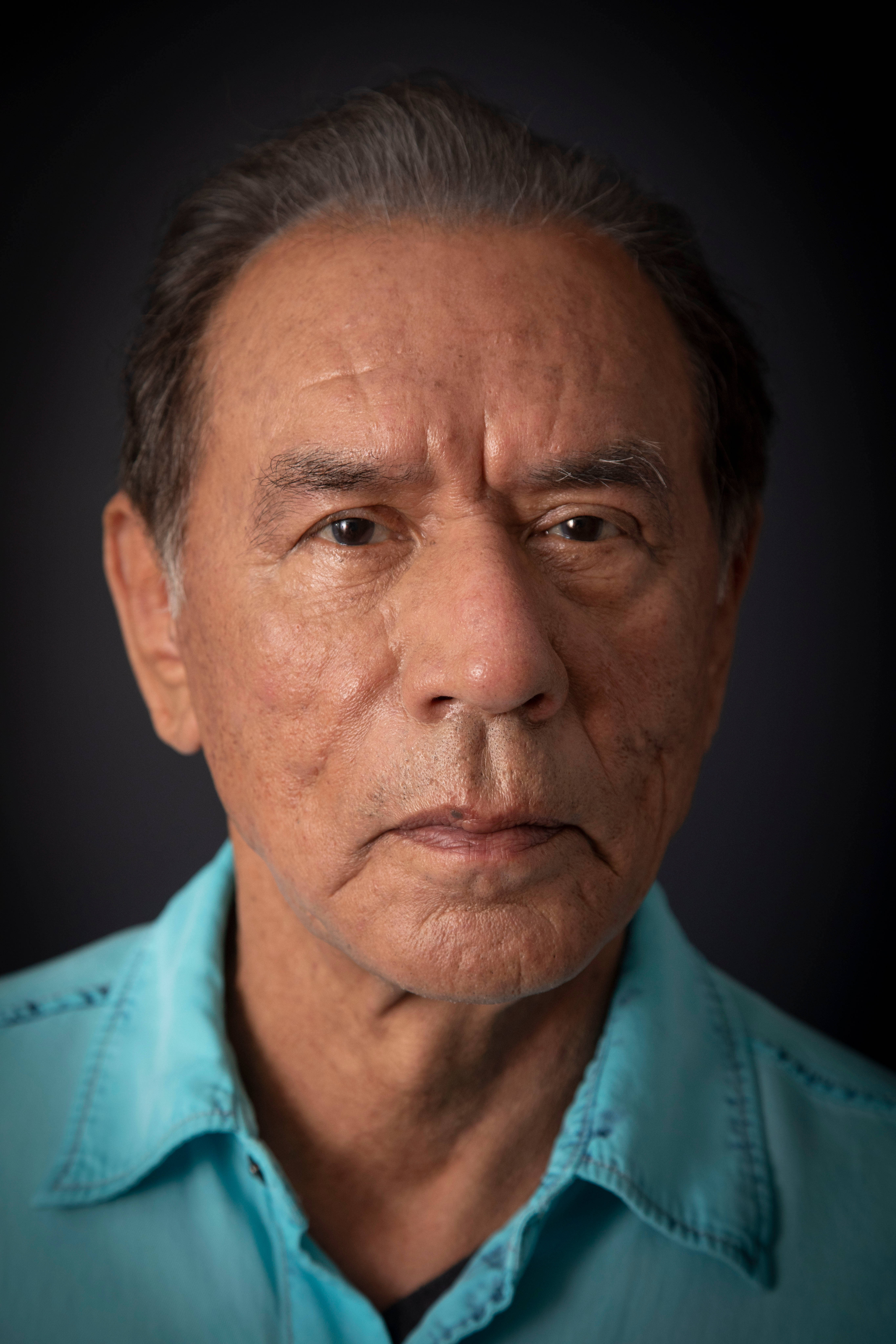 actor 桌布 壁紙 — 一位灰白頭髮、滿臉皺紋的長者身穿青綠色襯衫，在深色背景下的特寫肖像。