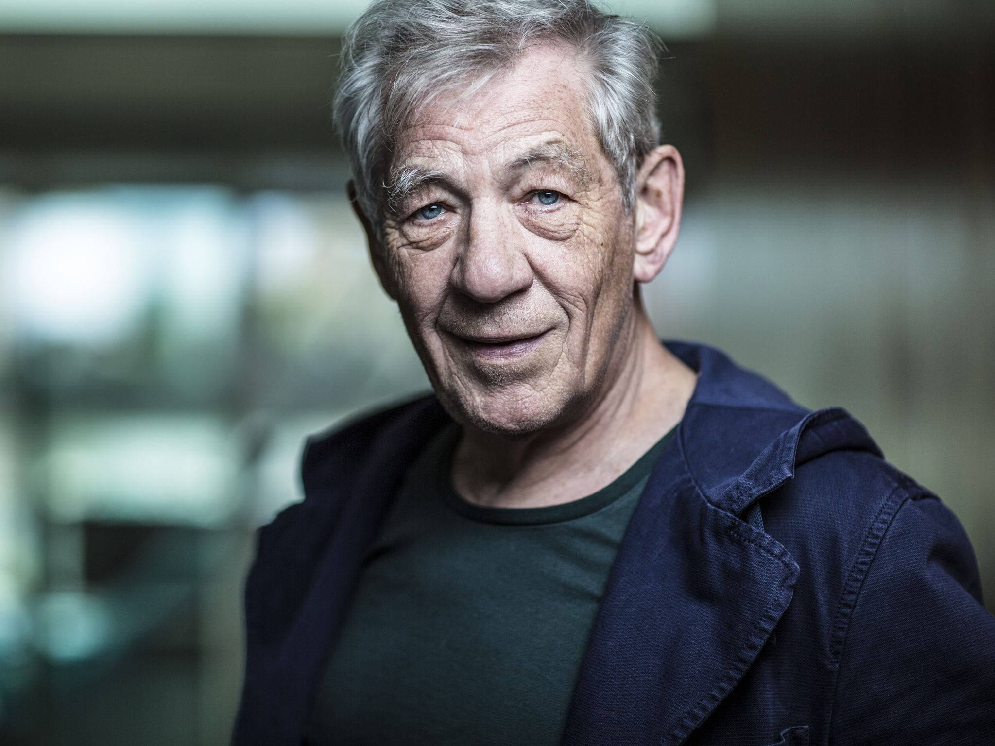 actor 桌布 壁紙 — 一位灰白頭髮、藍眼睛的長者近距離肖像，在柔和模糊的室內環境中溫暖微笑。