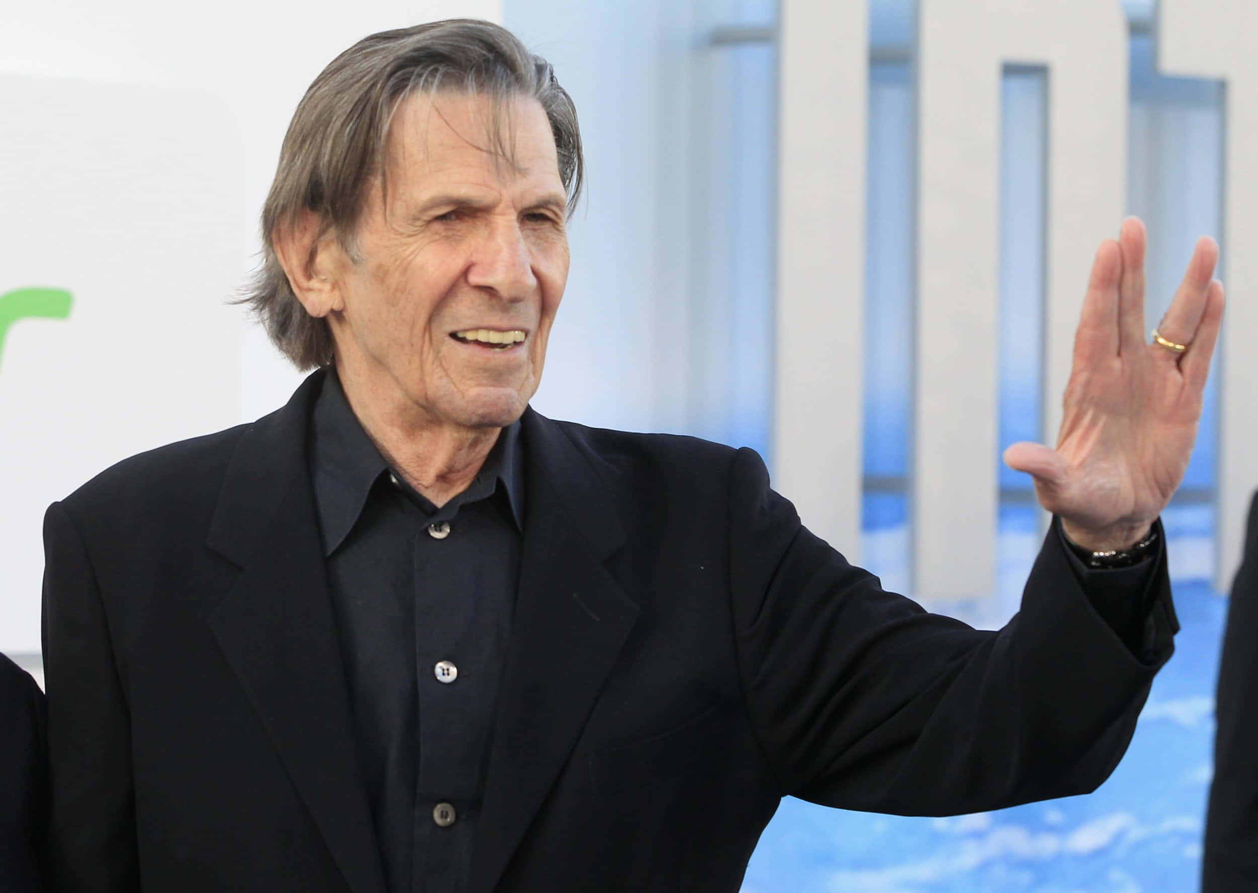 Celebrity 桌布 壁紙 — 一位灰白頭髮的老年男子穿著黑色西裝，在明亮背景的活動中愉快地揮手。