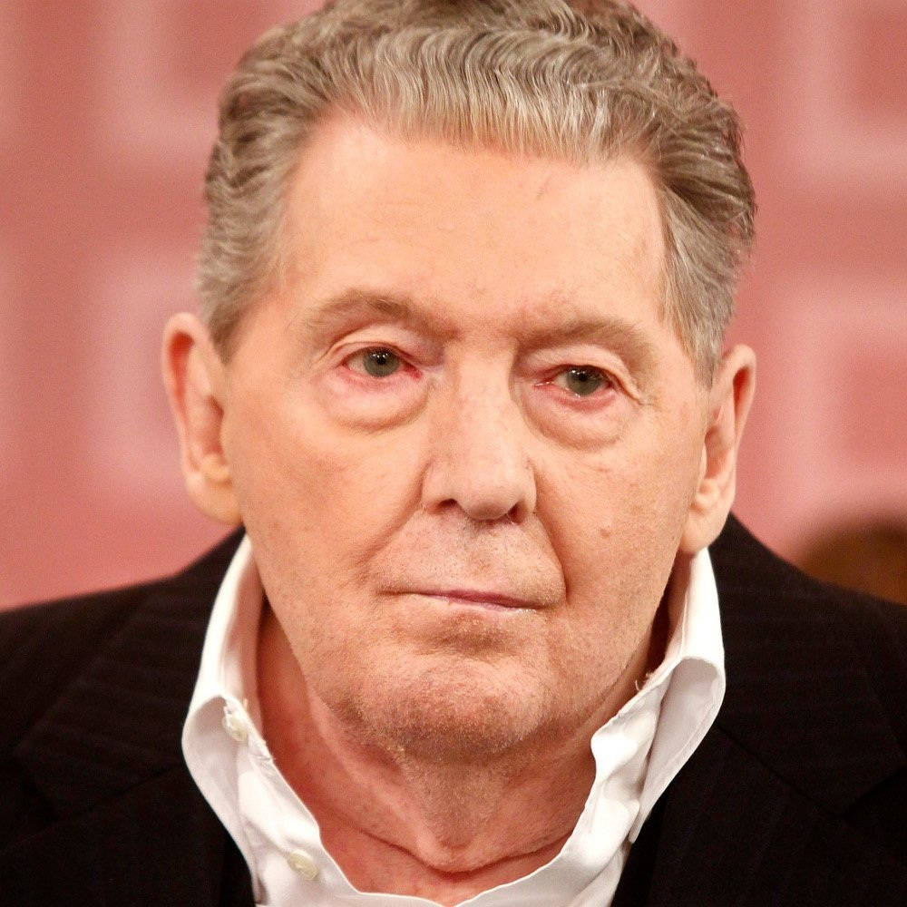 Jerry Lee Lewis 桌布 壁紙 — 一位灰白頭髮的老年男性穿著黑色西裝和白色襯衫，在柔和粉紅色背景前的特寫肖像。