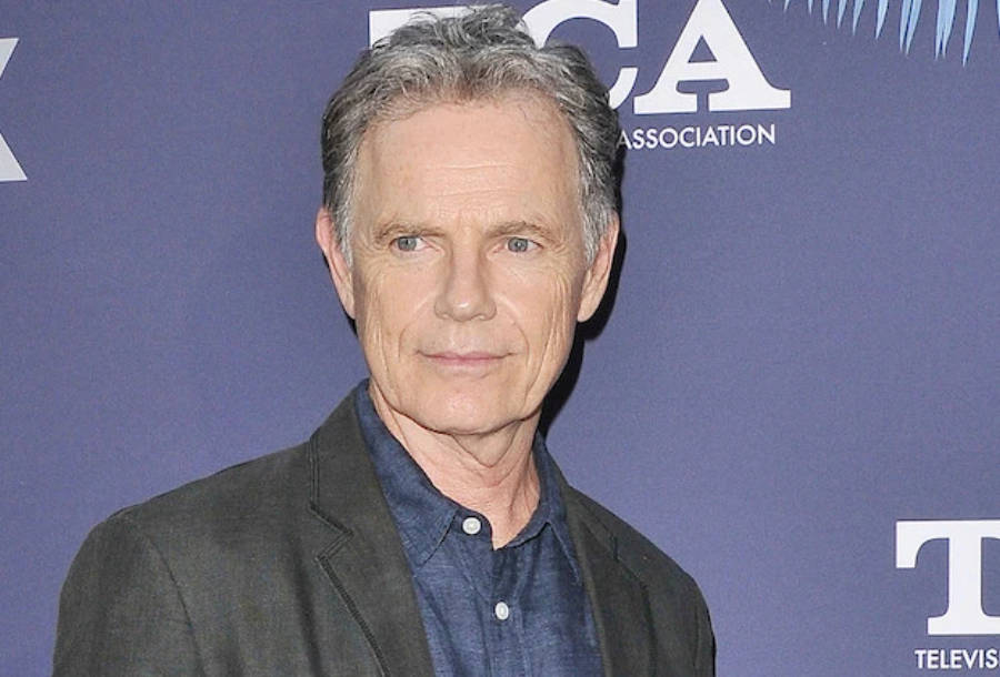 actor 桌布 壁紙 — 一位灰髮、表情平靜的中年男子站在帶有白色標誌的藍色活動背景前。