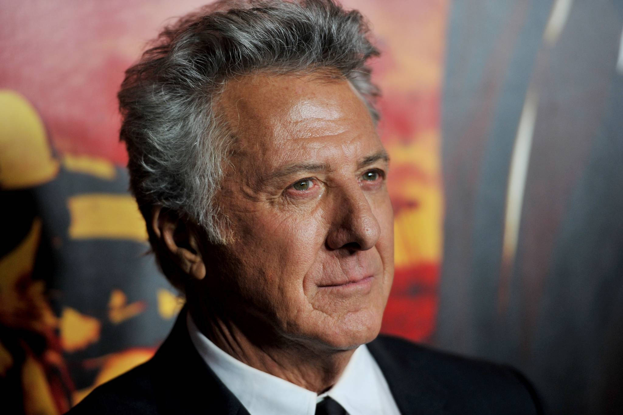 actor 桌布 壁紙 — 一位灰髮、身穿深色西裝、氣質出眾的年長男士的特寫肖像，背景為色彩繽紛的抽象圖案。