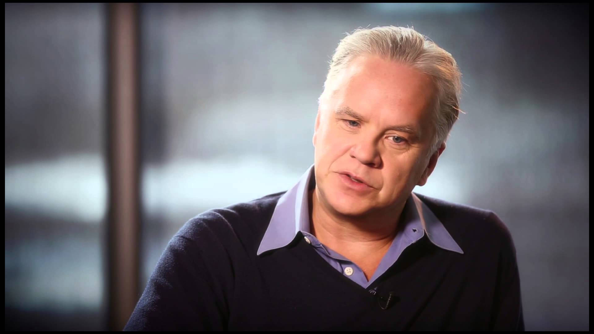 Celebrity 桌布 壁紙 — 一位灰髮中年男子穿著深色毛衣，內搭紫色有領襯衫，在室內說話。