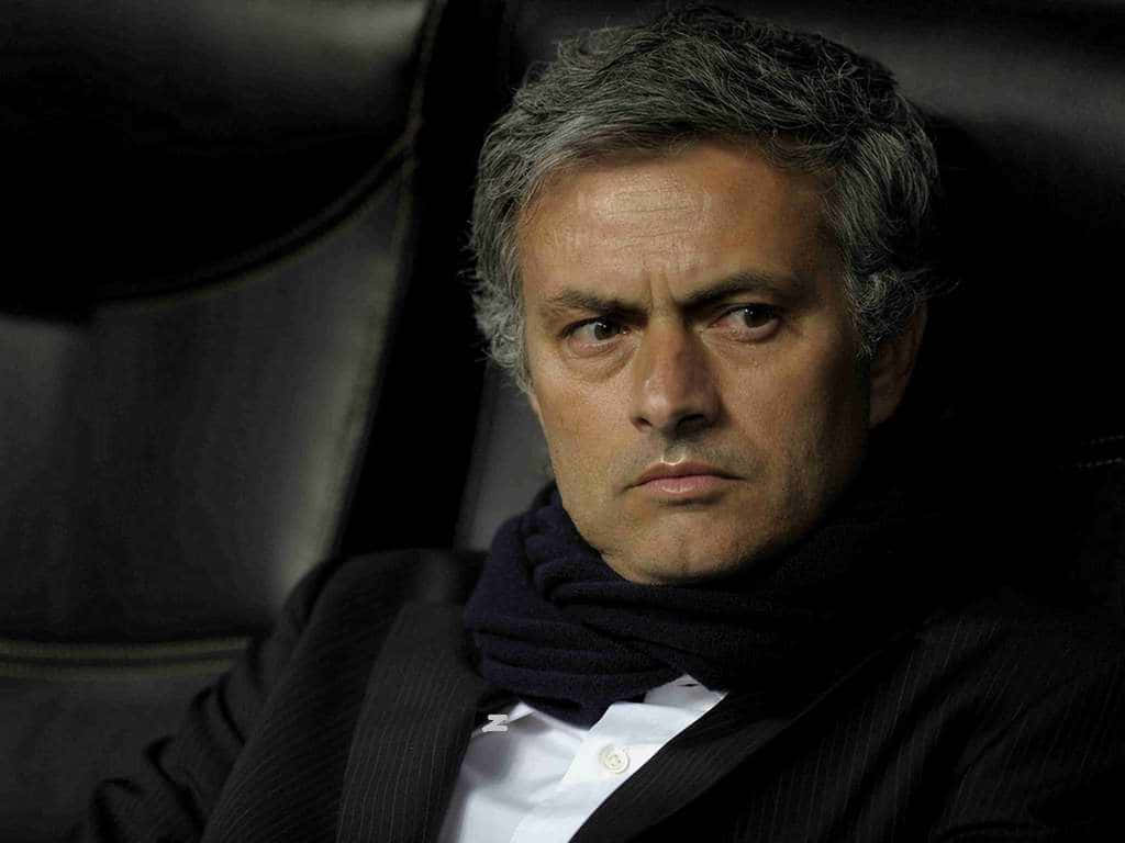 足球 桌布 壁紙 — 一位灰髮嚴肅男士的近照，身穿深色西裝和圍巾，坐在光線昏暗的體育館長椅上。