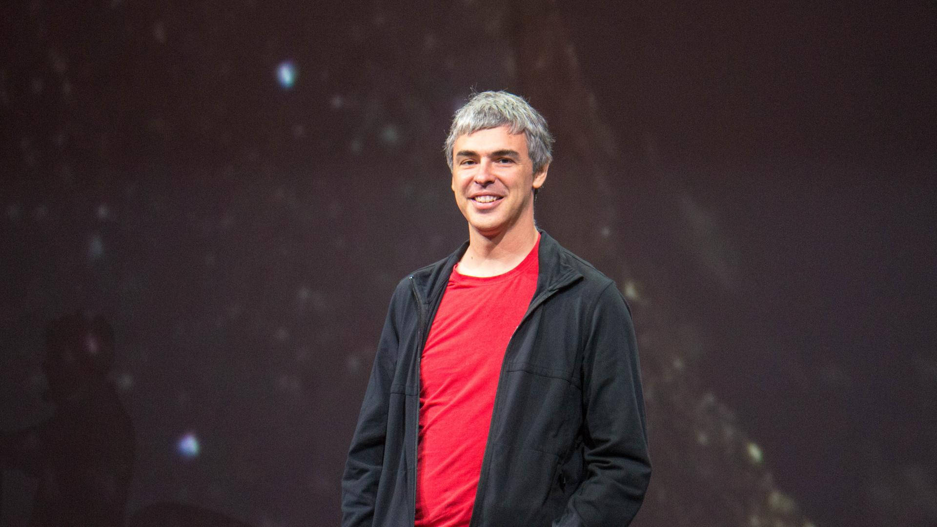 身穿紅色襯衫和黑色外套的男子在星空背景的舞台上微笑。 — Google Meet 壁紙