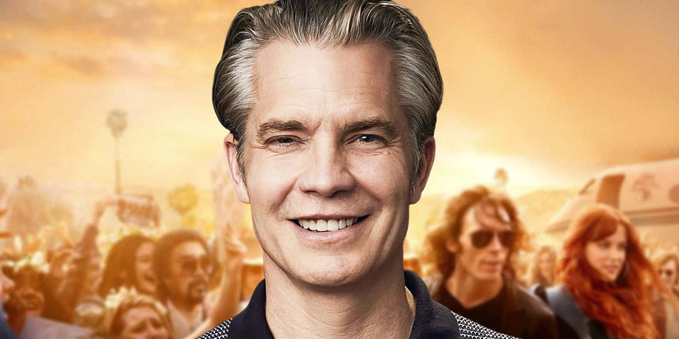 timothy olyphant 桌布 壁紙 — 一位灰髮微笑的男子站在金色戶外音樂會中模糊的人群前。