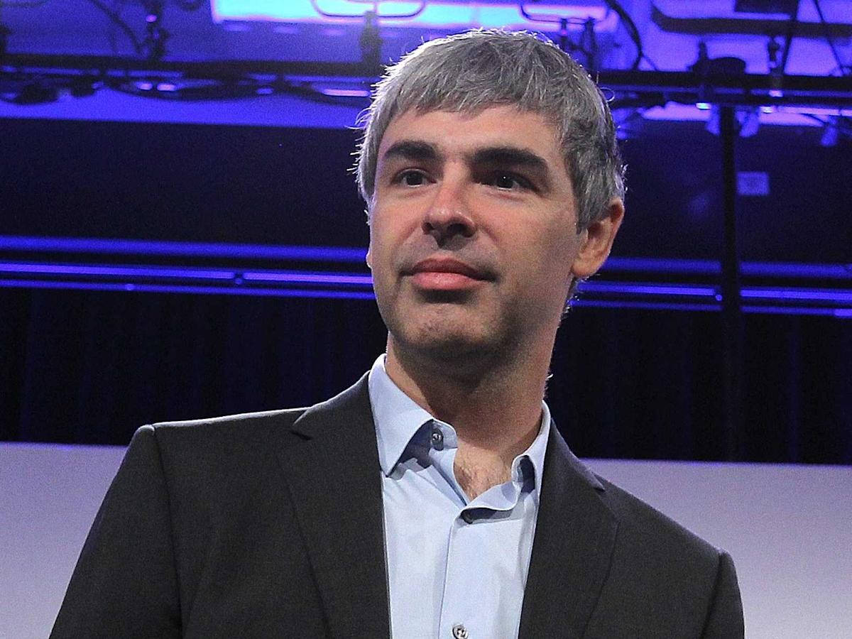 google 桌布 壁紙 — 一位灰髮男士身穿深色西裝和淺藍色襯衫，站在藍色舞台燈光下，上方可見懸掛裝置。