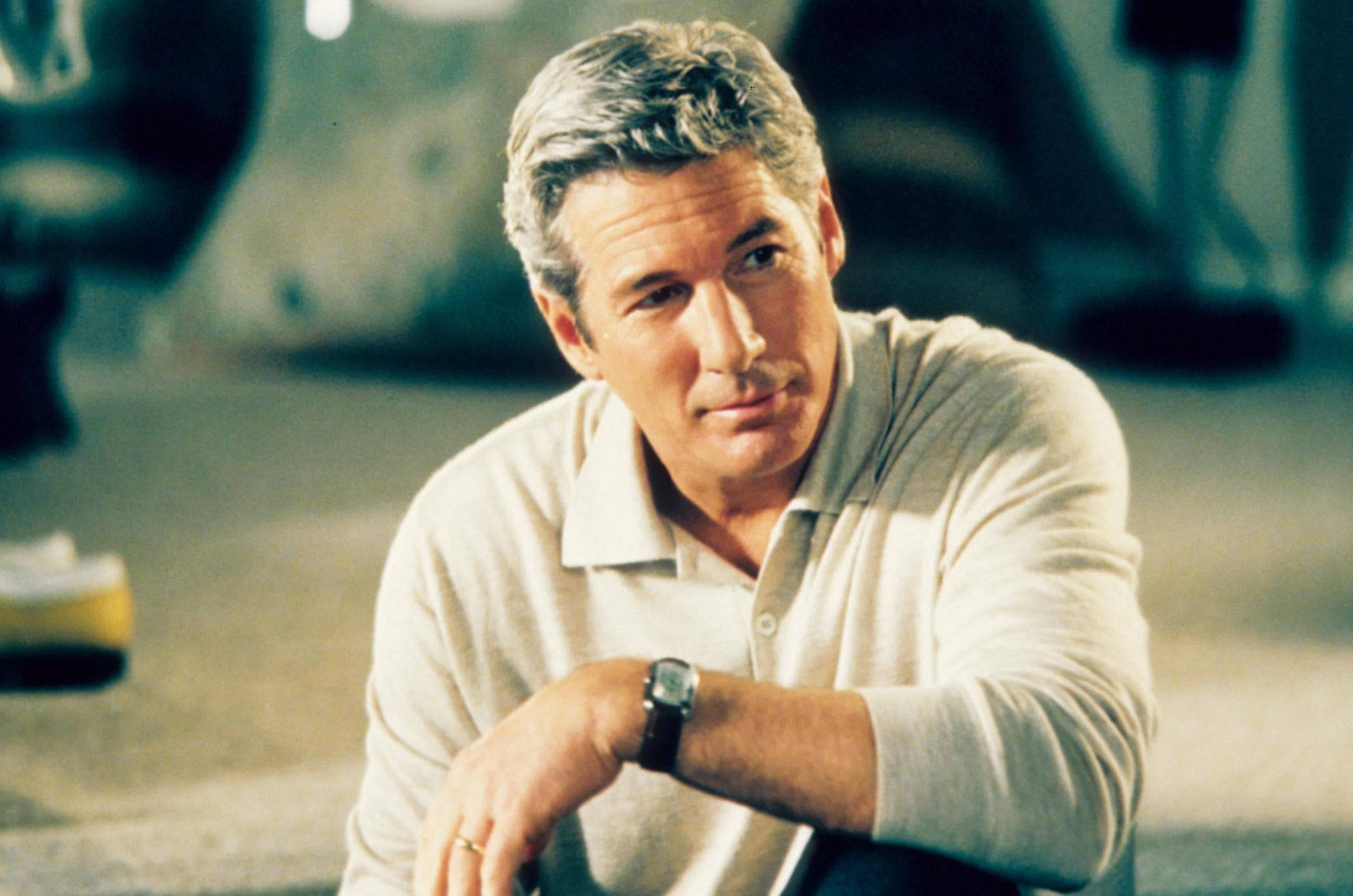 Richard Gere 桌布 壁紙 — 一位灰髮男子穿著淺色Polo衫，手腕戴著手錶，身體前傾，若有所思地看著相機。