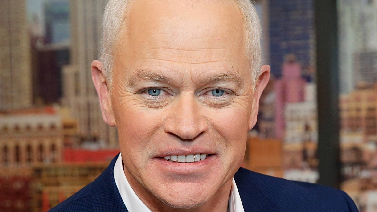 actor 桌布 壁紙 — 一位灰髮藍眼的微笑男士穿著深色西裝，背景是模糊的城市景觀的 close-up 肖像。
