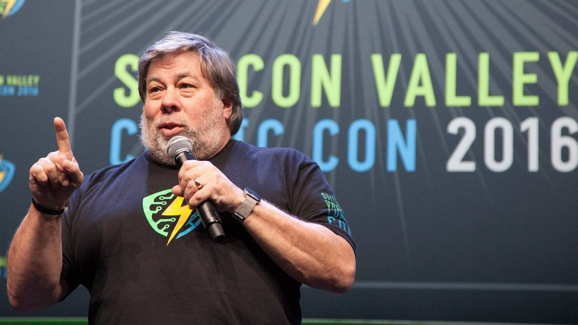 人像動態 桌布 壁紙 — 一位灰髮鬍鬚男士在Comic-Con Valley 2016活動中對著麥克風說話，同時另一隻手指向上方。