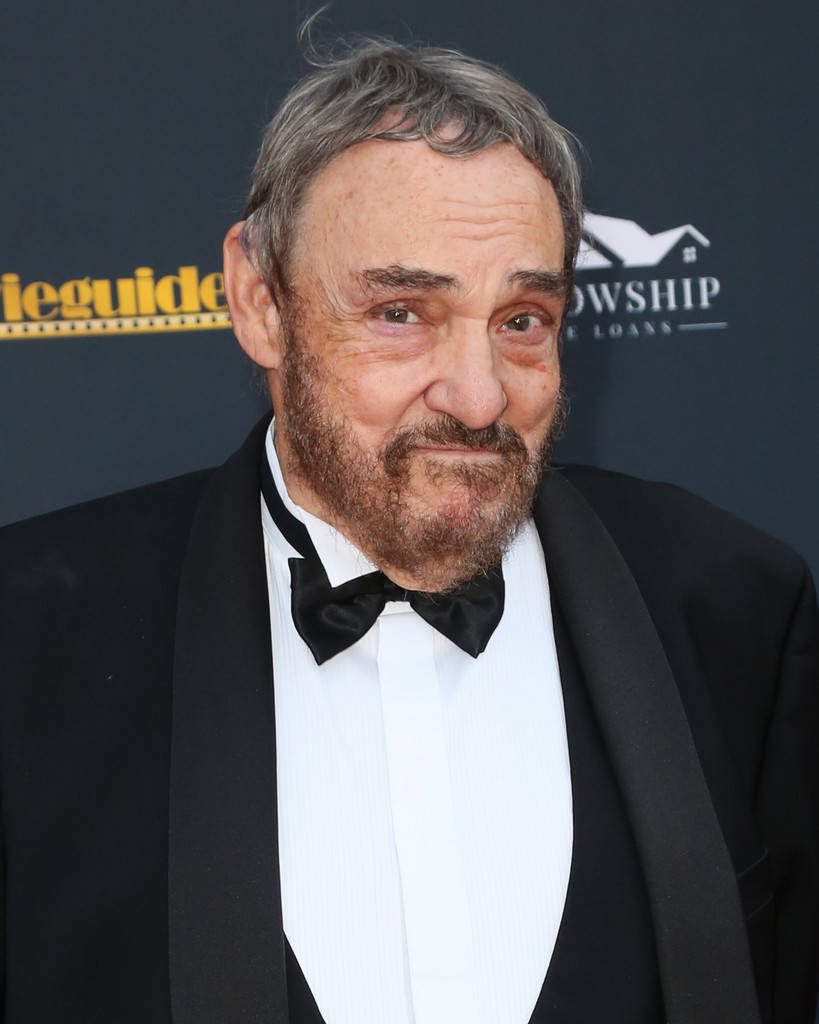 Celebrity 桌布 壁紙 — 一位灰髮鬍鬚男士身穿黑色燕尾服和領結，在帶有標誌的深色背景下的特寫肖像。