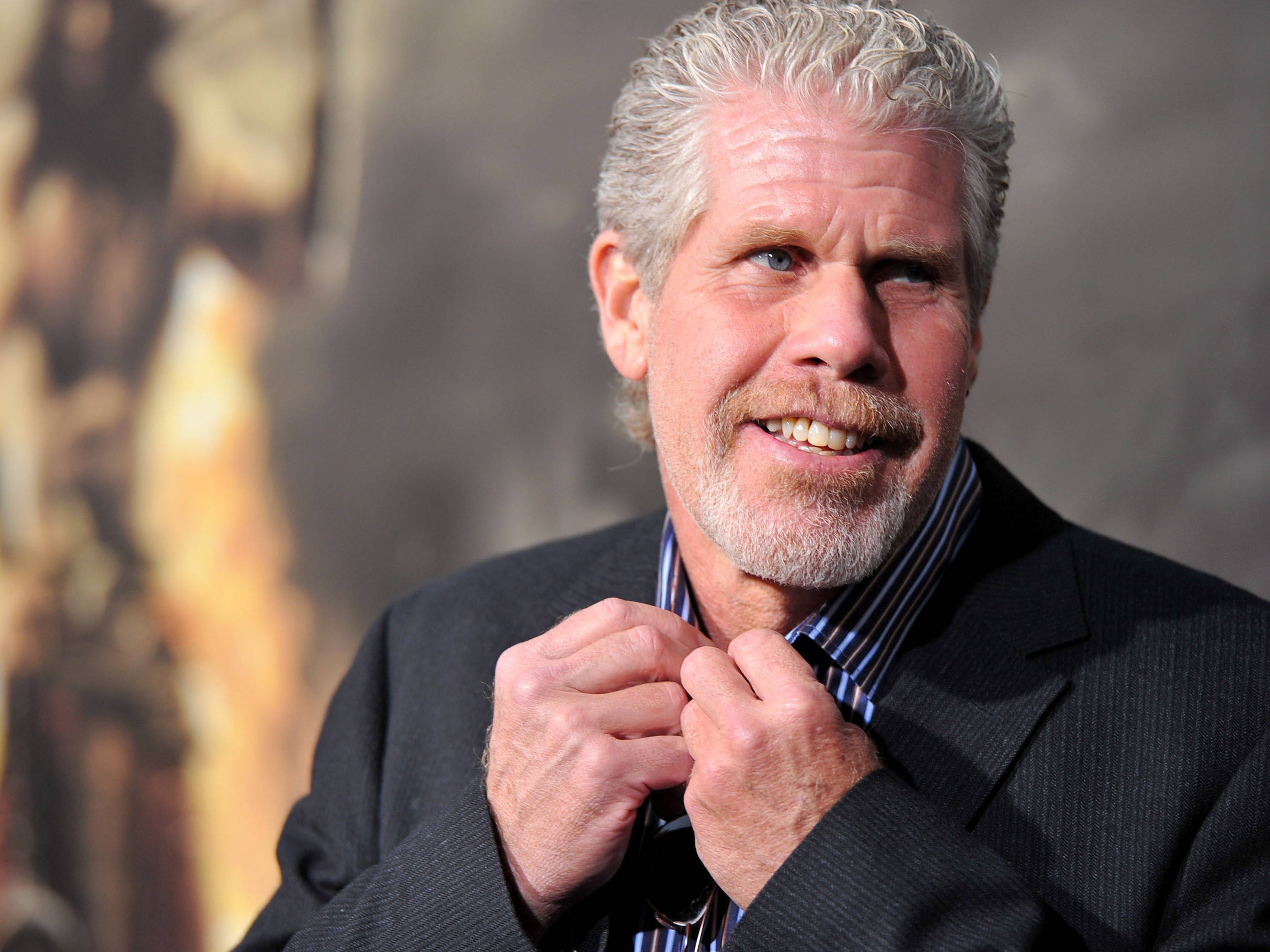 Celebrity 桌布 壁紙 — 一位灰髮鬍鬚的微笑男士在模糊的金色背景下調整領帶。