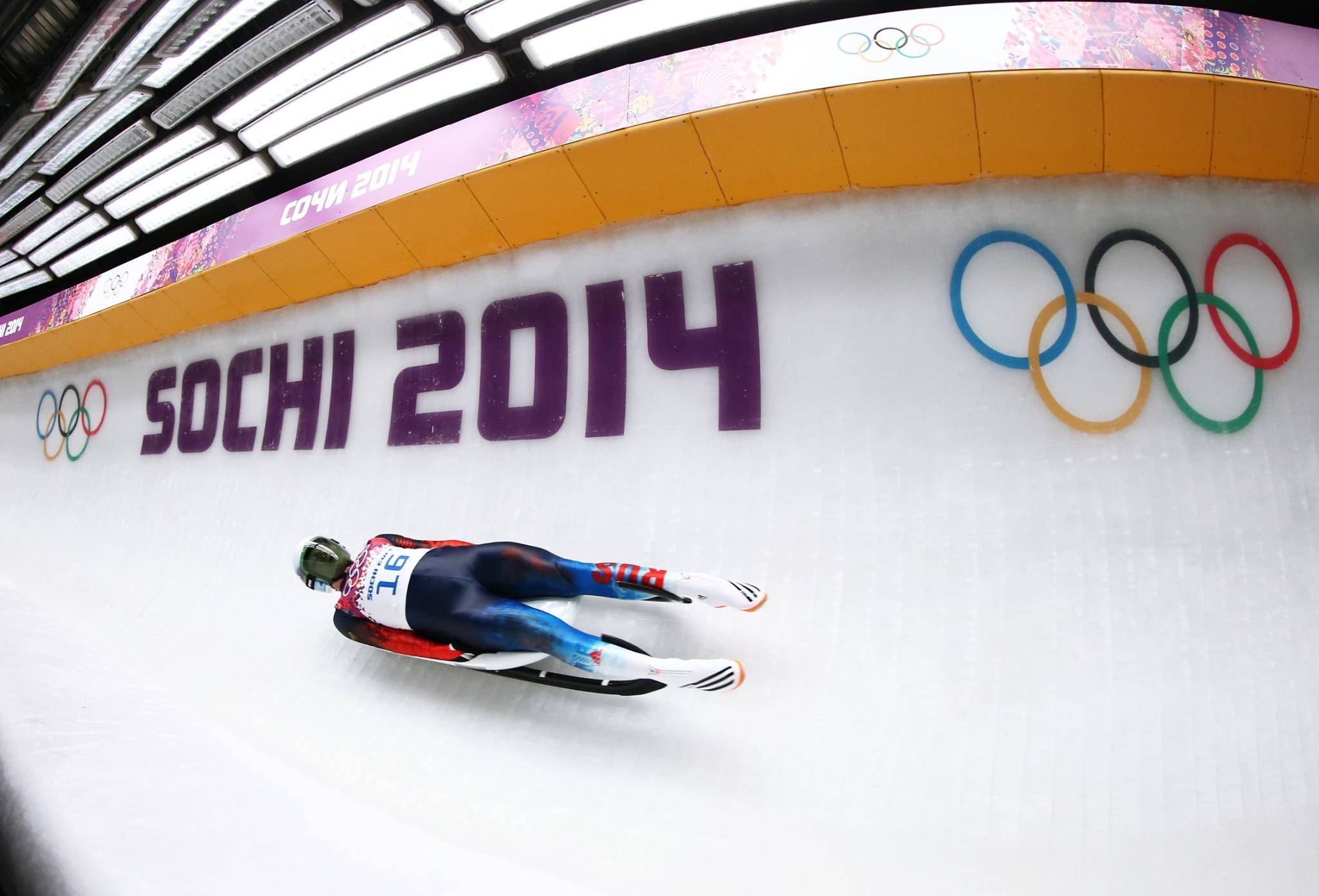 luge 桌布 壁紙 — 一位無舵雪橇運動員在2014年索契冬季奧運會上高速滑下雪道，奧運五環清晰可見。