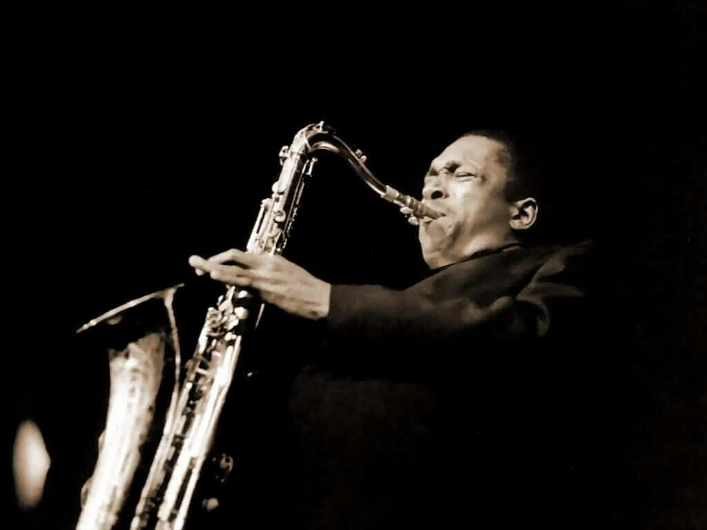 Jazz 桌布 壁紙 — 一位爵士音樂家在黑暗背景下，於戲劇性的舞台燈光下熱情地演奏薩克斯風。