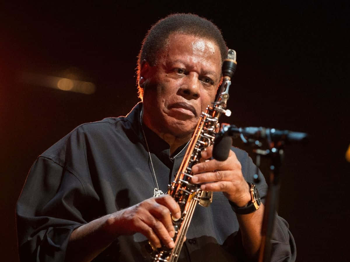 Wayne Shorter 桌布 壁紙 — 一位爵士音樂家在黑暗背景下於溫暖的舞台燈光下熱情地演奏薩克斯風。