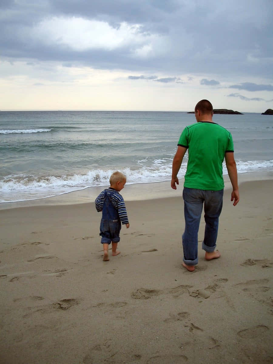 Beach Walk 桌布 壁紙 — 一位父親和幼兒在陰天下赤腳走在沙灘上，海浪翻滾而來。