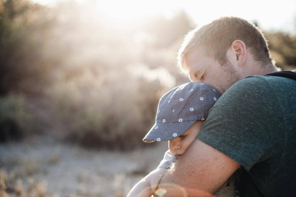 Very Cute Baby 桌布 壁紙 — 一位父親溫柔地擁抱他的孩子，金色的陽光透過他們身後模糊的沙漠景觀照射進來。