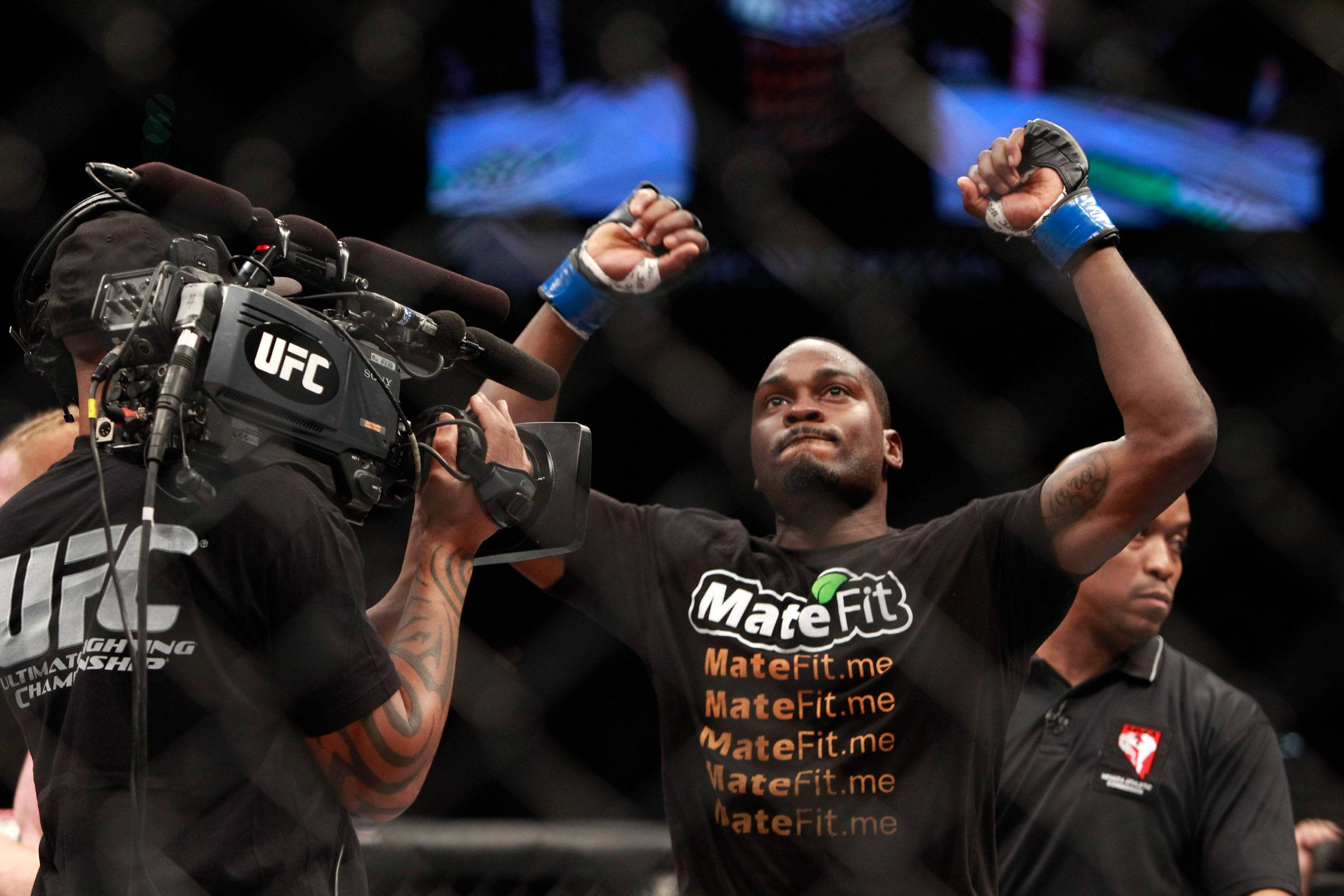 Champion 桌布 壁紙 — 一位獲勝的UFC拳手在八角籠內高舉拳頭慶祝勝利，同時有攝影師為他拍攝。
