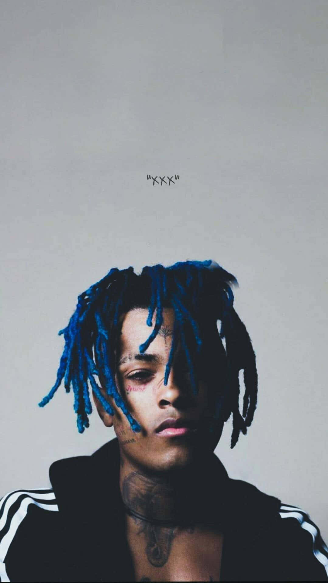 XXXTENTACION 桌布 壁紙 — 一位男士的肖像，擁有充滿活力的藍色辮子和刺青，背景為純灰色。