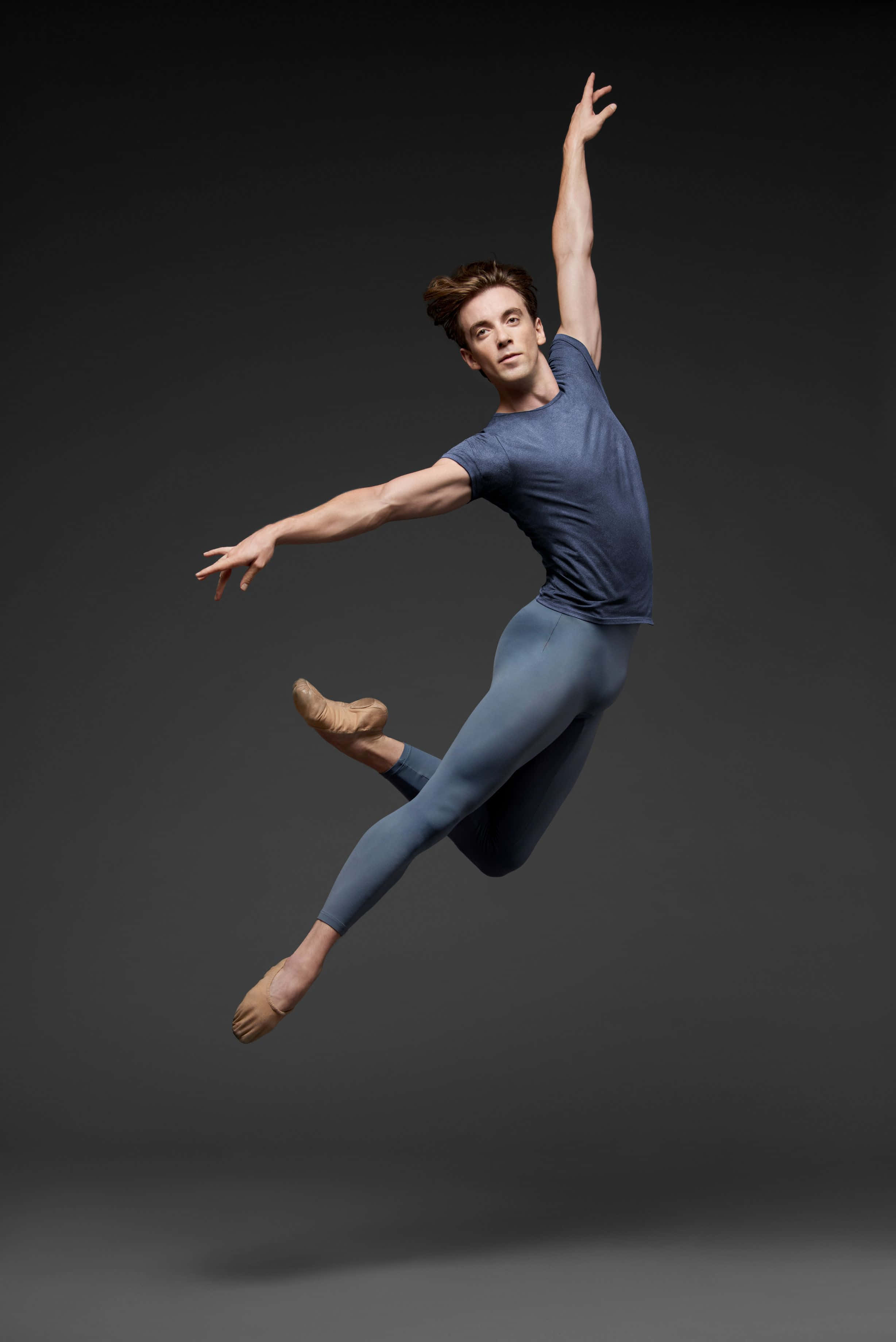 dancer 桌布 壁紙 — 一位男性芭蕾舞者在黑暗的攝影棚背景下穿著藍色緊身衣和足尖鞋優雅地騰空跳躍。
