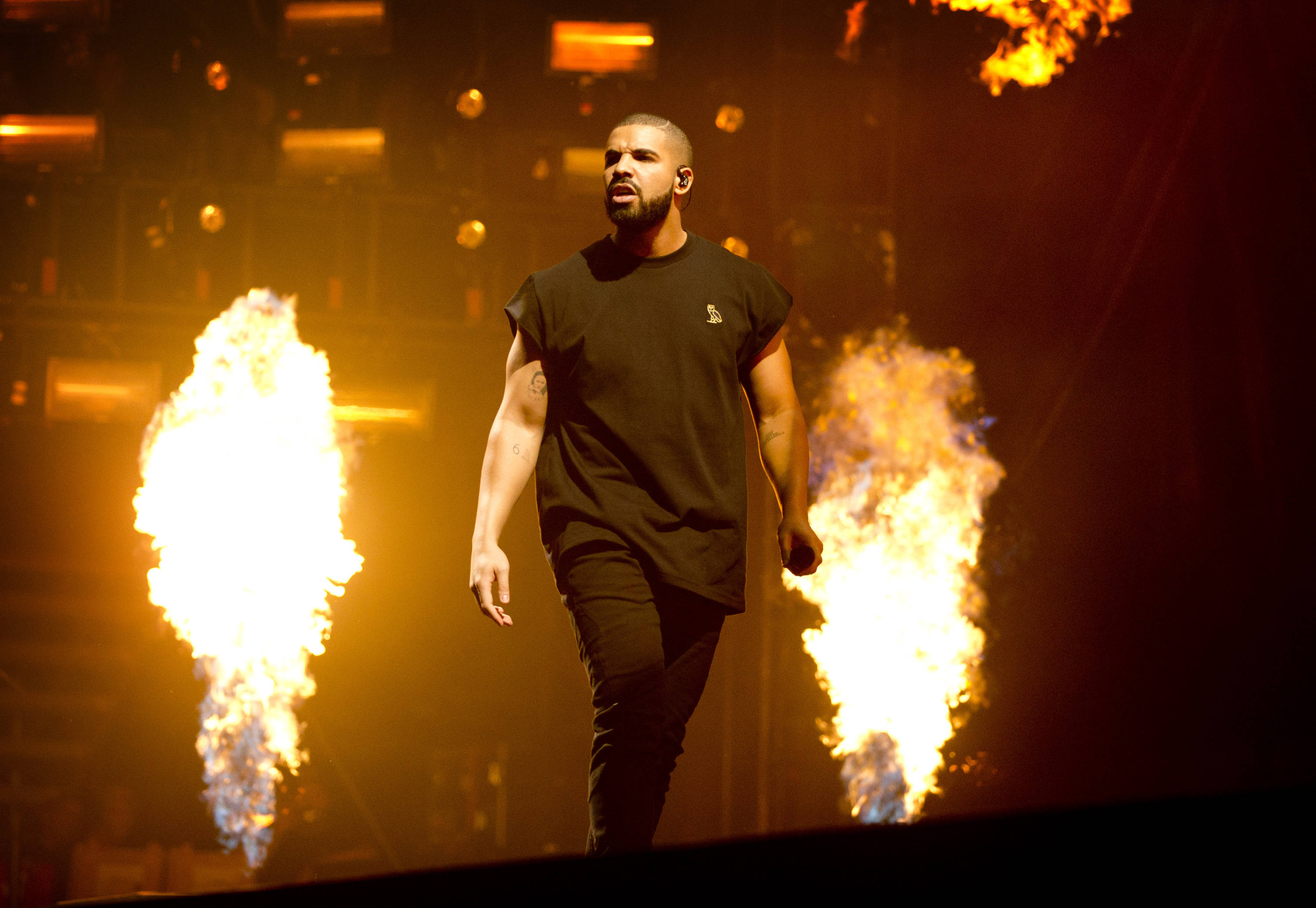 Drake 桌布 壁紙 — 一位男性表演者在溫暖的舞台燈光下，自信地走在被咆哮火焰包圍的舞台上。