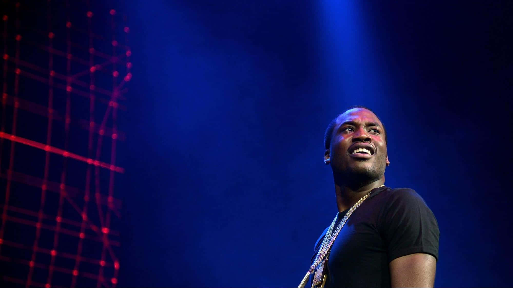 Meek 桌布 壁紙 — 一位男性表演者在藍色舞台燈光下熱情微笑，背景有紅色雷射網格圖案。