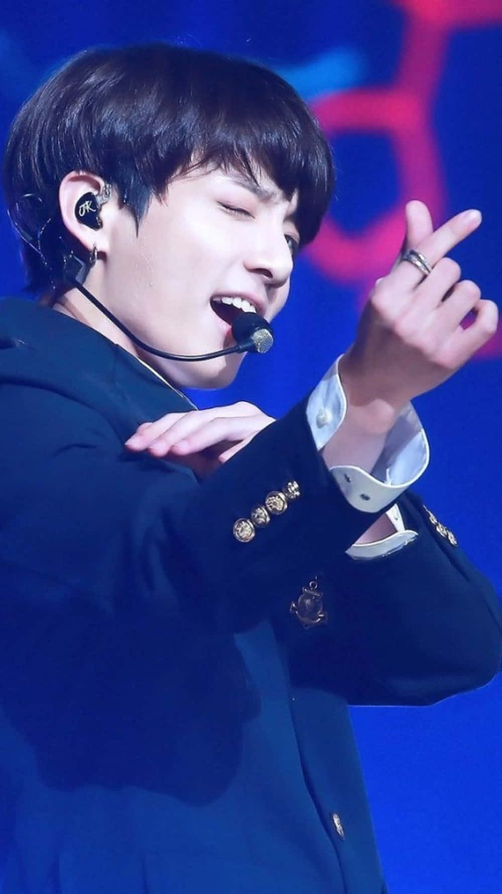 BTS 桌布 壁紙 — 一位男性表演者在藍色舞台燈光下穿著深色西裝外套熱情地唱歌。
