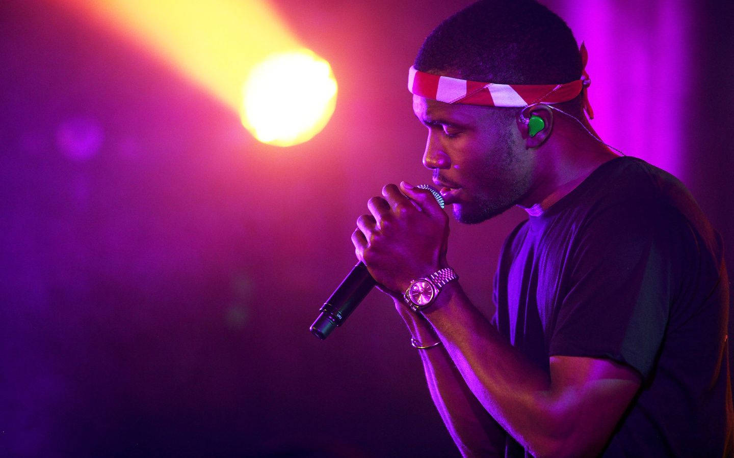 Frank Ocean 桌布 壁紙 — 一位男歌手在充滿活力的紫色和黃色舞台燈光下，熱情地對著麥克風演唱。