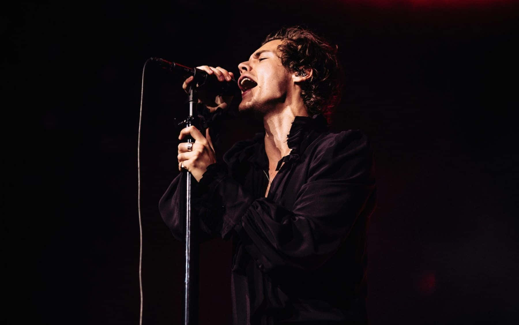 Harry Styles Black And White 桌布 壁紙 — 一位男歌手在戲劇性的紅光下閉著眼睛、張開嘴巴，熱情地在舞台上表演。