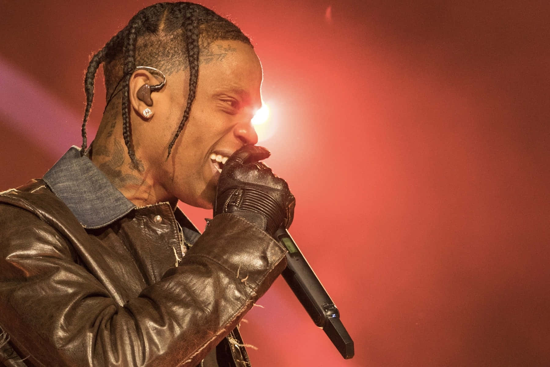 Travis Scott Concert 桌布 壁紙 — 一位男饒舌歌手，梳著辮子頭，身上有刺青，在紅色舞台燈光下對著麥克風熱情演唱。