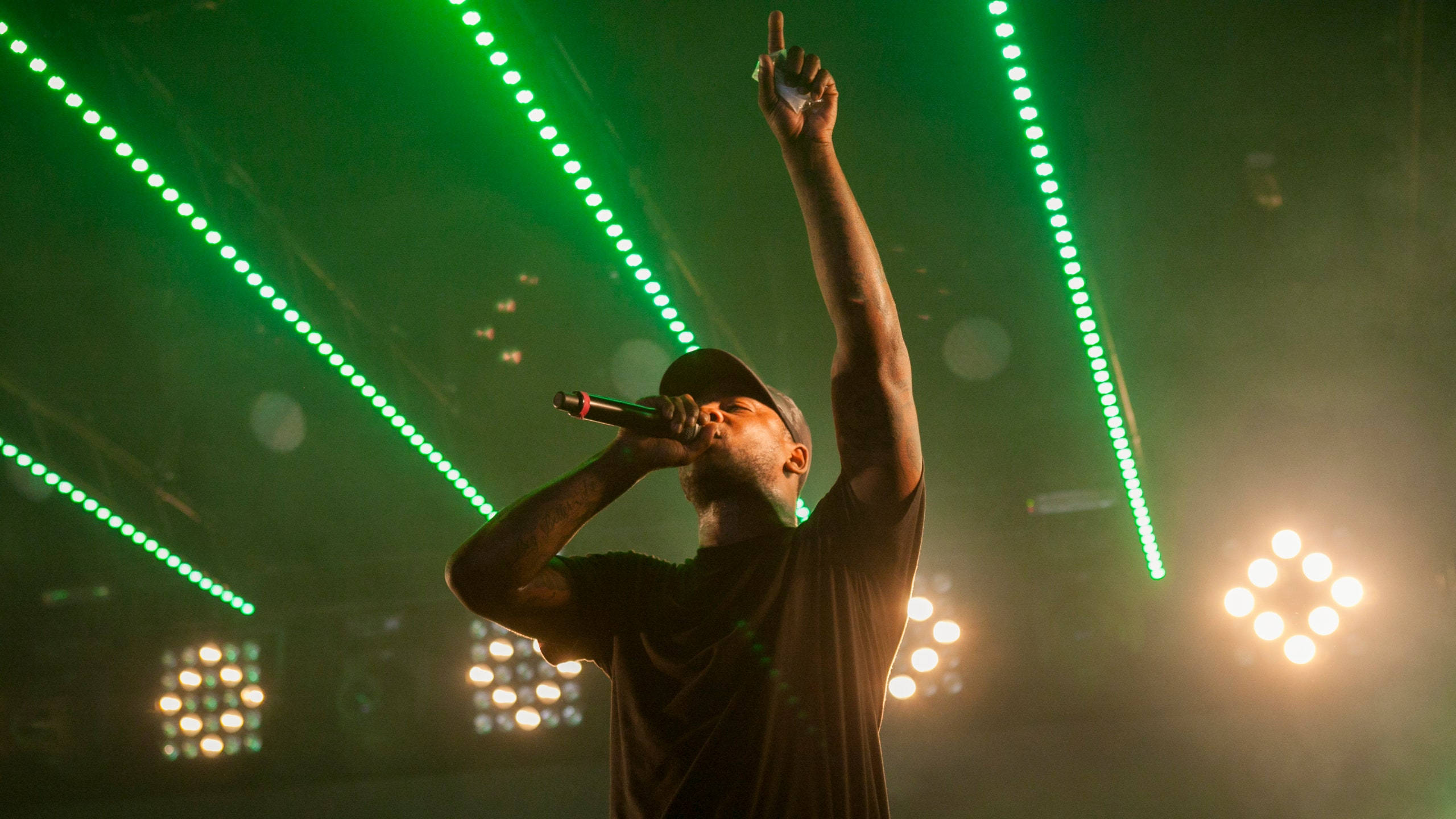 Skepta 桌布 壁紙 — 一位男饒舌歌手在充滿活力的綠色雷射燈光和溫暖的聚光燈下熱情地表演。