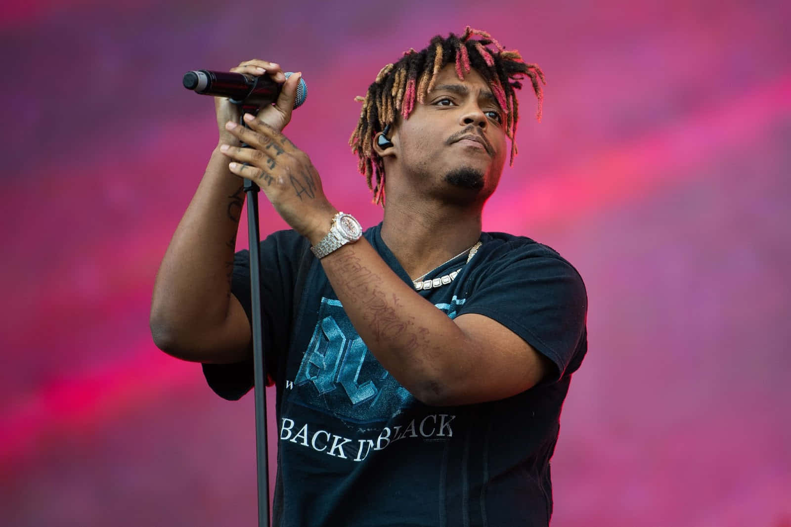 饒舌歌手在舞台上表演，留著色彩繽紛的辮子和麥克風 — Juice Wrld 壁紙