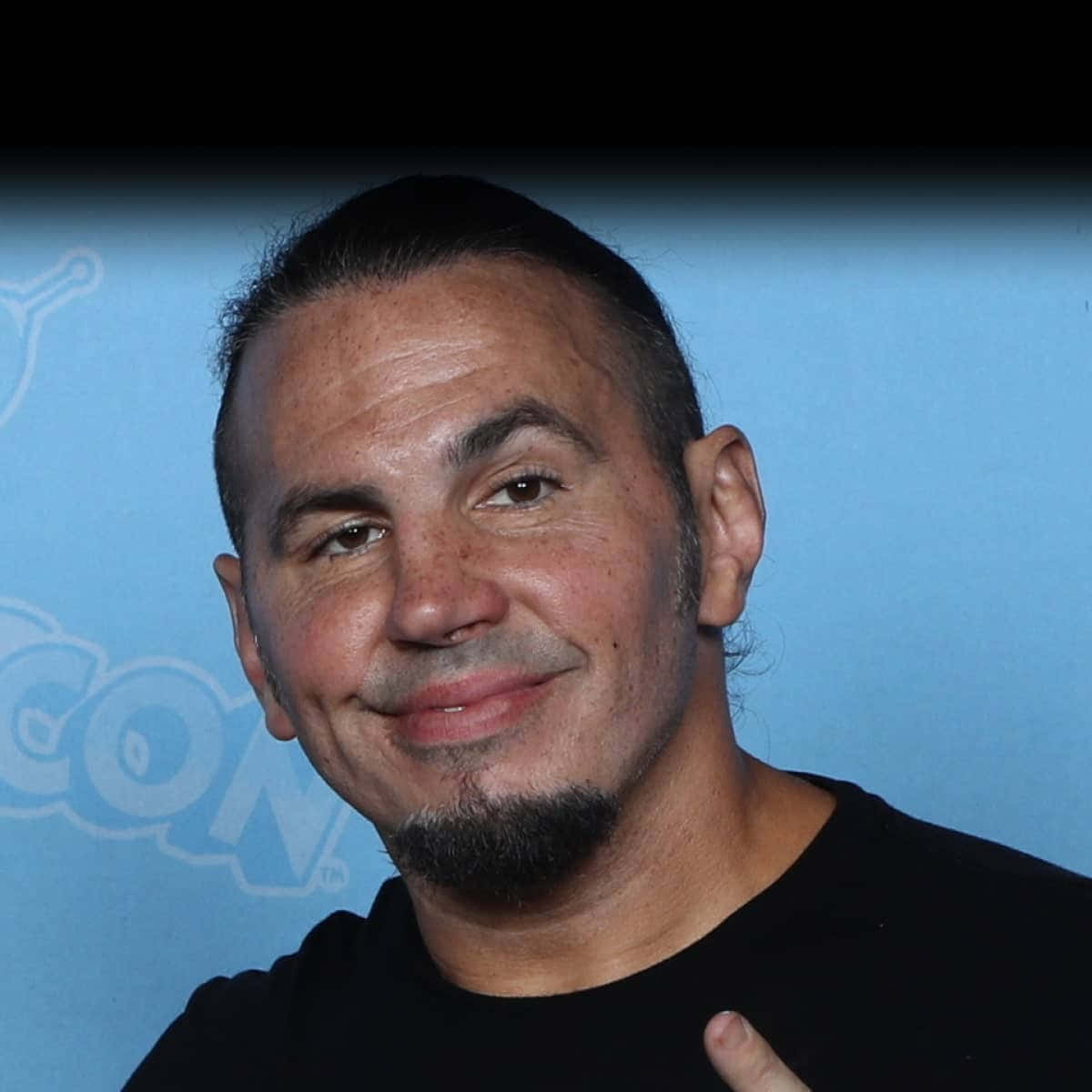 WWE 桌布 壁紙 — 一位留山羊鬍的男人在藍色Comic-Con背景前溫暖微笑。